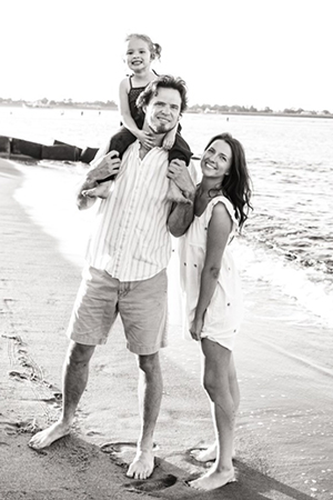 A father, mother, and young daughter smiling and happy at the beach.